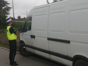 zdjęcie przedstawia policjanta kontrolującego pojazd koloru białego typu bus